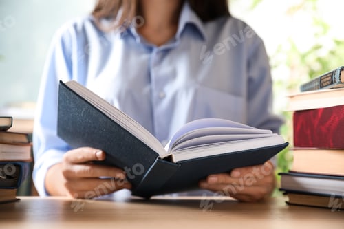 Preview: Woman reading hardcover book at wooden table indoors, closeup