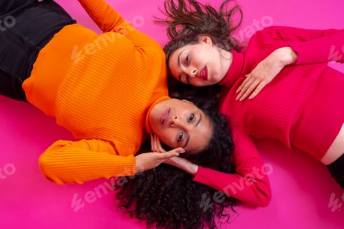 Preview: Two multi-ethnic women lying in a trendy posing on a pink background, lifestyle