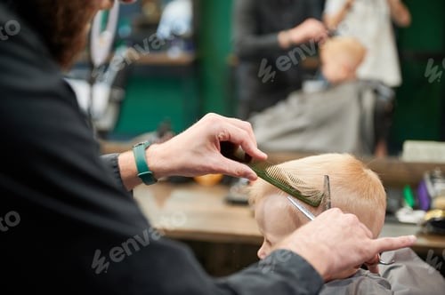 Preview: Behind shoulder view of male barber cutting little boy's hair.