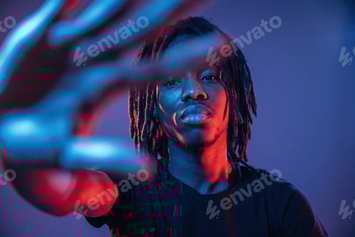 Preview: With hand in front of him, stop gesture. African American guy is studio with neon lighting