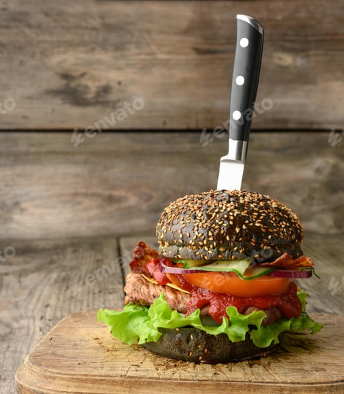 Preview: Cheeseburger with black bun, meat and vegetables on a wooden background