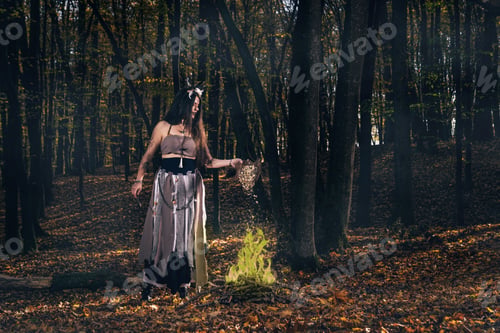 Preview: Young female with long hair and face paint in a witch costume casting a spell in a forest