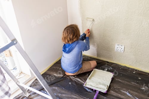 Preview: Eight year old boy using paint roller to paint a house wall
