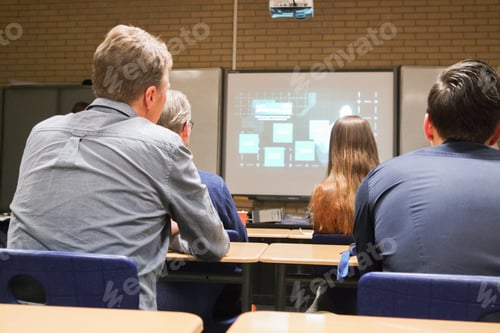 Preview: People from behind in the class are watching presentation on the board.