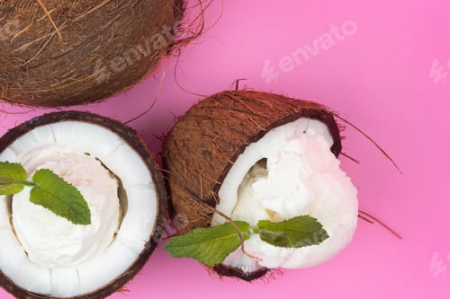Preview: Vanilla ice cream balls in fresh coconut halves decorated with mint leaves on a pink background