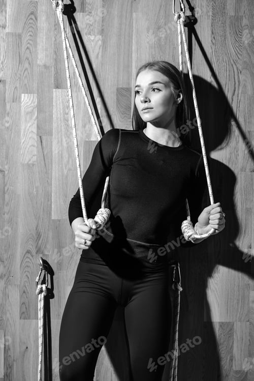 Preview: Black and white photo of a slim girl dressed in a black sportswear is standing next to the rope