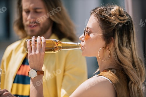 Preview: side view of young woman in sunglasses drinking cold beer at sunny day