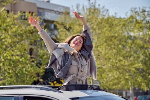 Preview: Joyful woman standing with arms raised in car sunroof