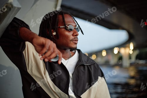 Preview: Young Adult Black Man Wearing Sunglasses Relaxing under Urban Bridge