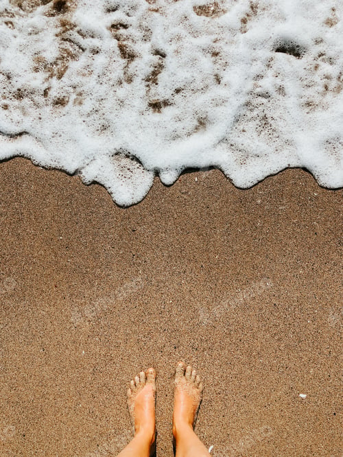 Preview: Woman legs barefoot at sea foam waves on sand beach summer day. top view above women feet.