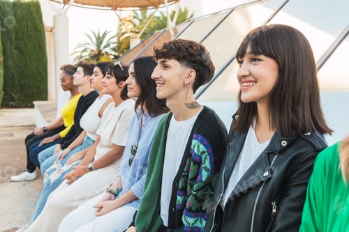 Preview: Happy young ethnic woman sitting with diverse friends in daylight near glass wall