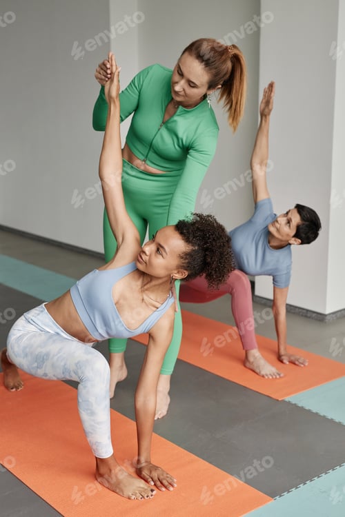 Preview: Female Yoga Instructor Assisting Women Stretching in Studio