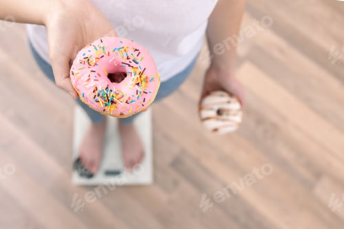 Preview: A woman stands on the scales, holds donuts in her hands, top view, copy space.