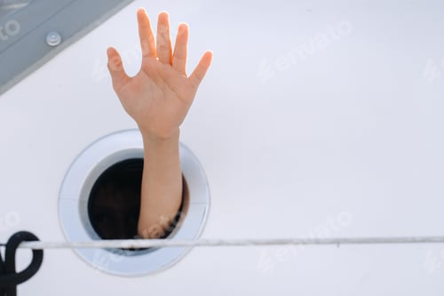 Preview: A man's hand sticks out of the porthole window on a ship at sea