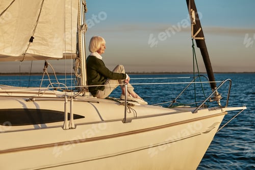 Preview: Senior relaxed woman sitting on the side of sailboat or yacht deck floating in the