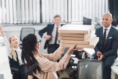 Preview: young businesswoman showing pizza boxes to happy colleagues in open space office