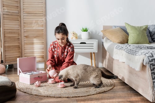 Preview: preteen girl sitting on floor and playing with toy tea set and cat
