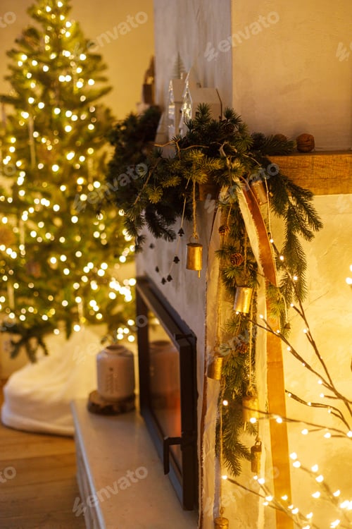Preview: Stylish christmas decorated fireplace mantel with fir branch, bells, ribbon and garland light