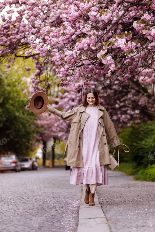 Preview: young beautiful stylish woman in hat and pink dress walking near sakura flowers in the park. Spring