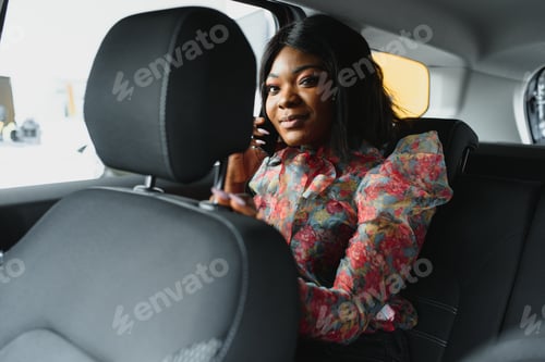Preview: Afro girl talking on phone, sitting in car on back seat and smiling, copy space