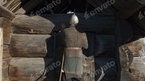 Preview: Rear view of an ancient russian bogatyr in chain armour and helmet coming to wooden old house. Media