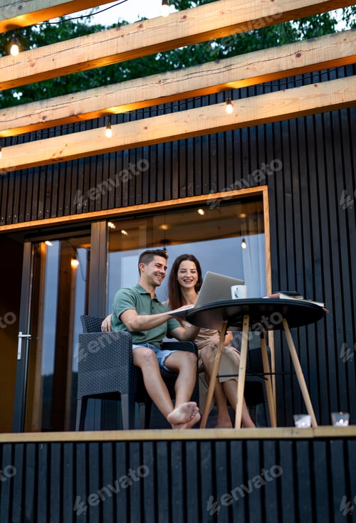 Preview: Young couple with laptop outdoors, weekend away in container house in countryside