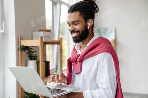 Preview: Happy african american guy in earphones working with laptop