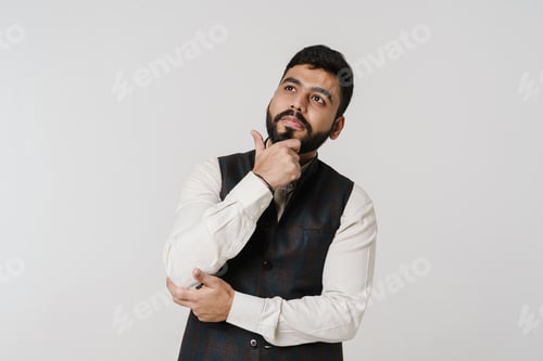Preview: Bearded south asian man holding his chin and looking upward