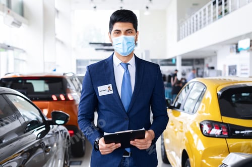 Preview: Salesman middle-eastern man in face mask posing in auto showroom