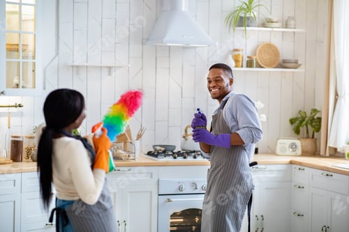 Preview: Young black couple fighting playfully with cleaning supplies while tidying their kitchen