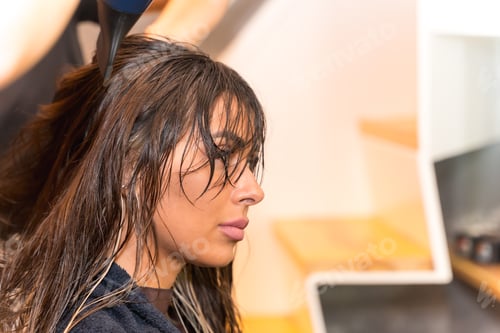 Preview: A brunette girl sitting in the beauty salon drying her hair with the dryer, hairdressing