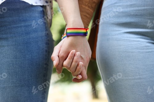 Preview: LGBT concept. Women in rainbow wristbands holding hands outdoors, closeup