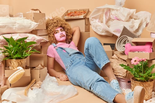 Preview: Tired young woman lies around cardboard boxes rests after unpacking belongings moves in new dwelling