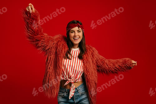 Preview: Fashionable young hipster woman wearing fluffy coat and dancing on red background