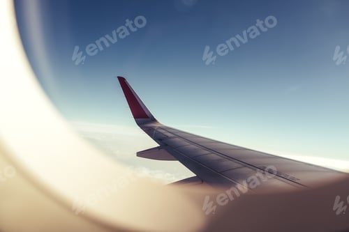 Preview: An airplane wing through airplane window with blue sky background