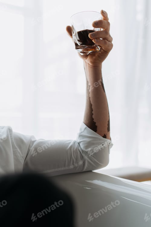 Preview: Cropped view of african american man with vitiligo in shirt holding glass of whiskey in bathtub