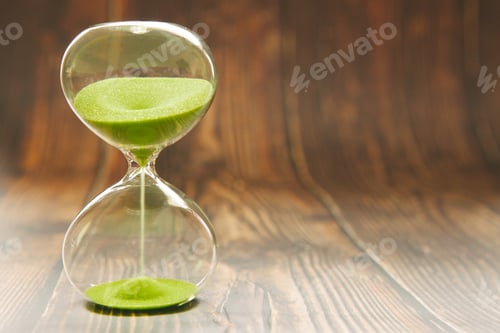 Preview: Hourglass with falling sand inside a glass bulb on a wooden daylight background