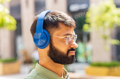 Preview: indian student with blue headset and backpack well looking at sunny day