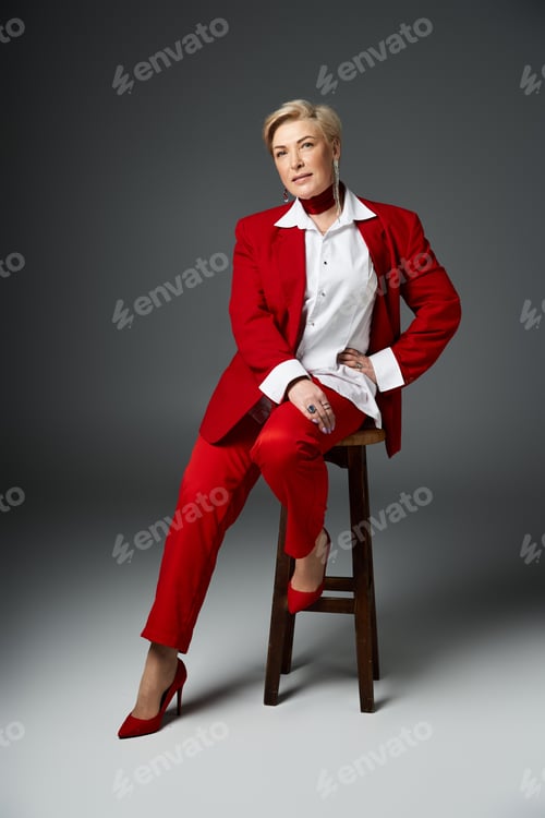 Preview: A confident woman in a chic red suit showcases modern fashion in the studio