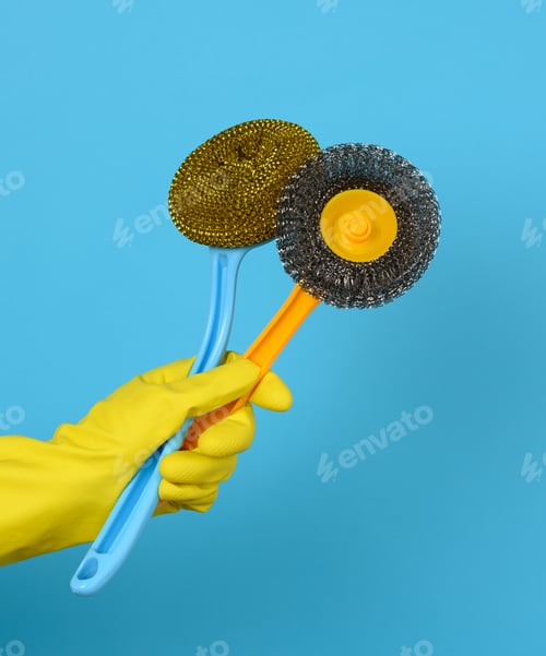Preview: Hand in a yellow glove holds a stack of plastic cleaning brushes, blue background