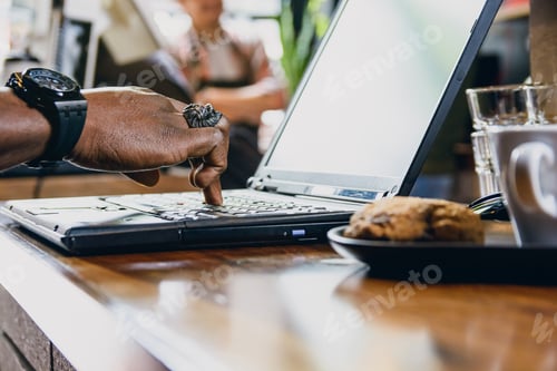 Preview: hand of unrecognizable black man touching with one finger laptop keyboard on table inside restaurant