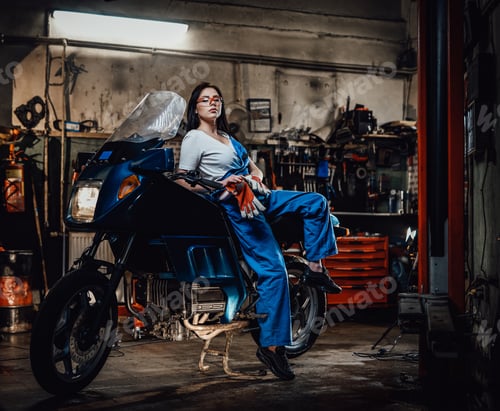 Preview: Hot brunette woman in blue overalls posing for a camera while leanign on sportbike
