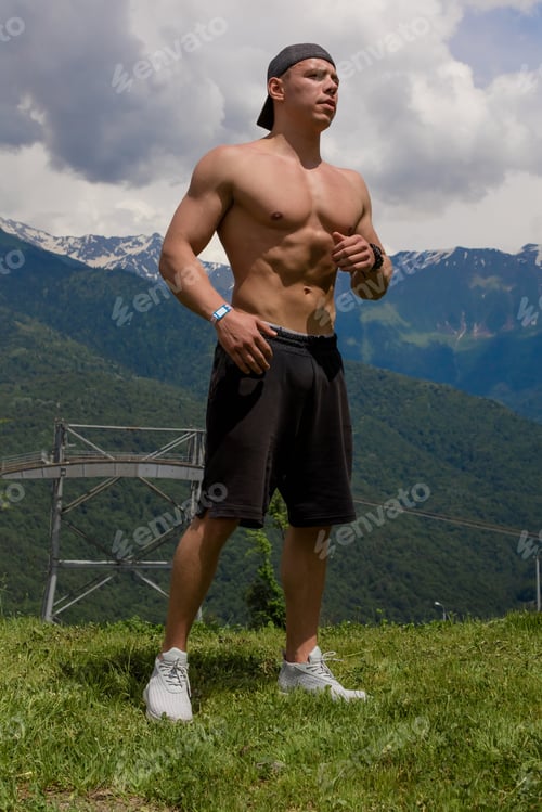 Preview: Bodybuilder posing in mountains. Handsome strong man showing his muscles.