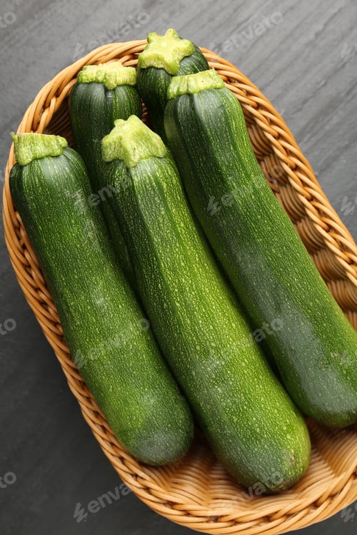 Preview: Fresh ripe zucchinis in wicker basket on black table, top view
