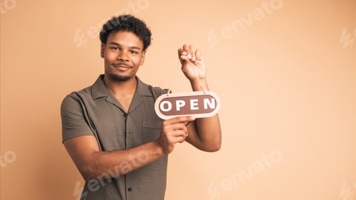 Preview: Smiling man with open sign inviting in beige studio