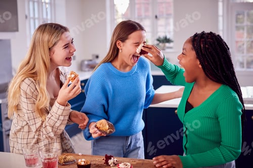 Preview: Group Of Teenage Girls Eating And Having Fun Playing With Cupcakes In Kitchen At Home