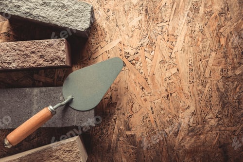 Preview: Construction brick and trowel at wooden background. Brick with mason on osb texture