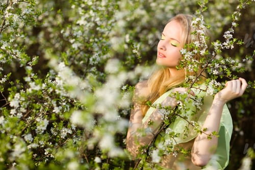 Preview: Young beautiful blond smiling woman in yellow dress standing in blooming cherry trees and looking at