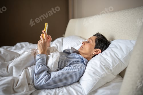 Preview: Calm drowsy apathetic woman in bed scrolling smartphone. Social media check, chat in morning relax