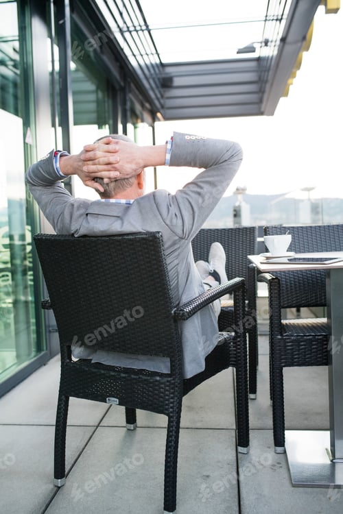 Preview: Senior businessman with a tablet in rooftop cafe